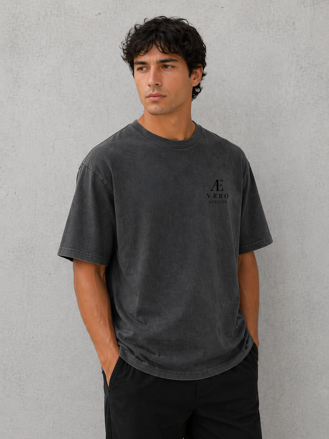 Man wearing a dark gray t-shirt with a logo on a plain background