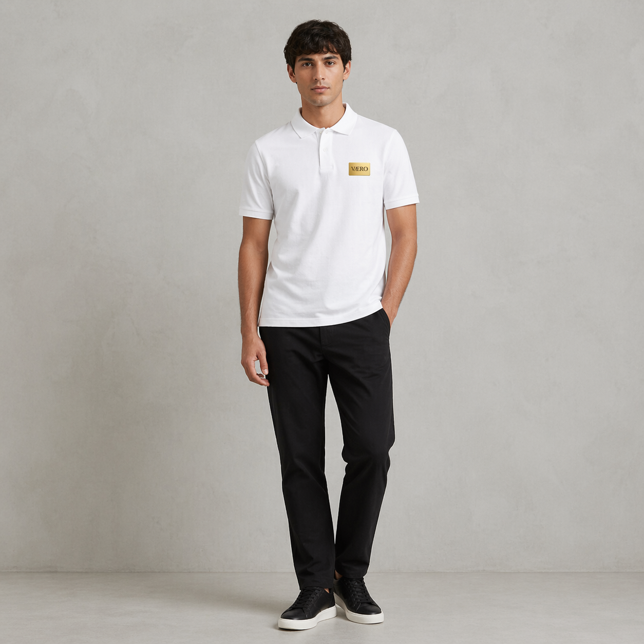 Man wearing a white polo shirt with a logo and black pants on a gray background