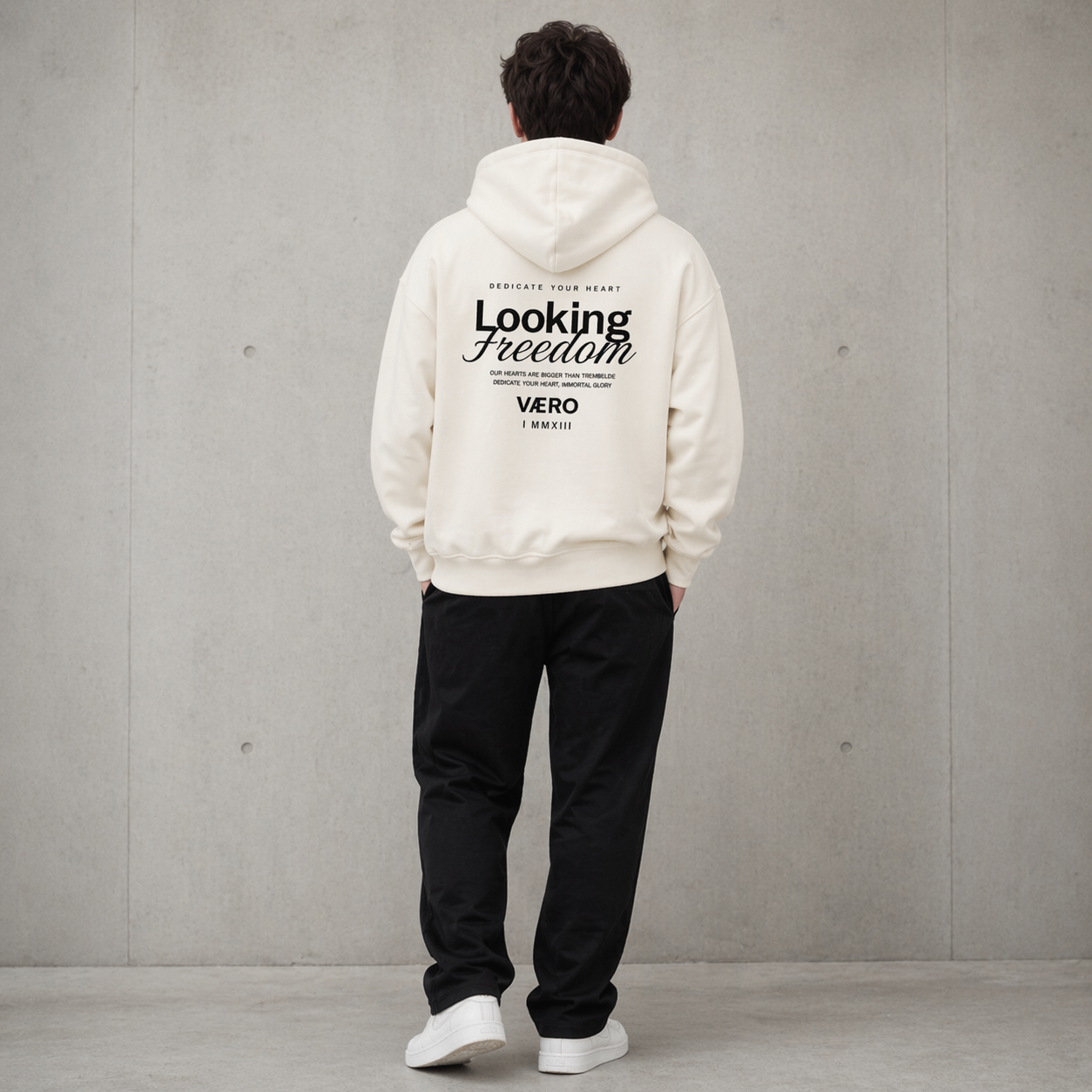 Person wearing a white hoodie with text on the back against a gray wall
