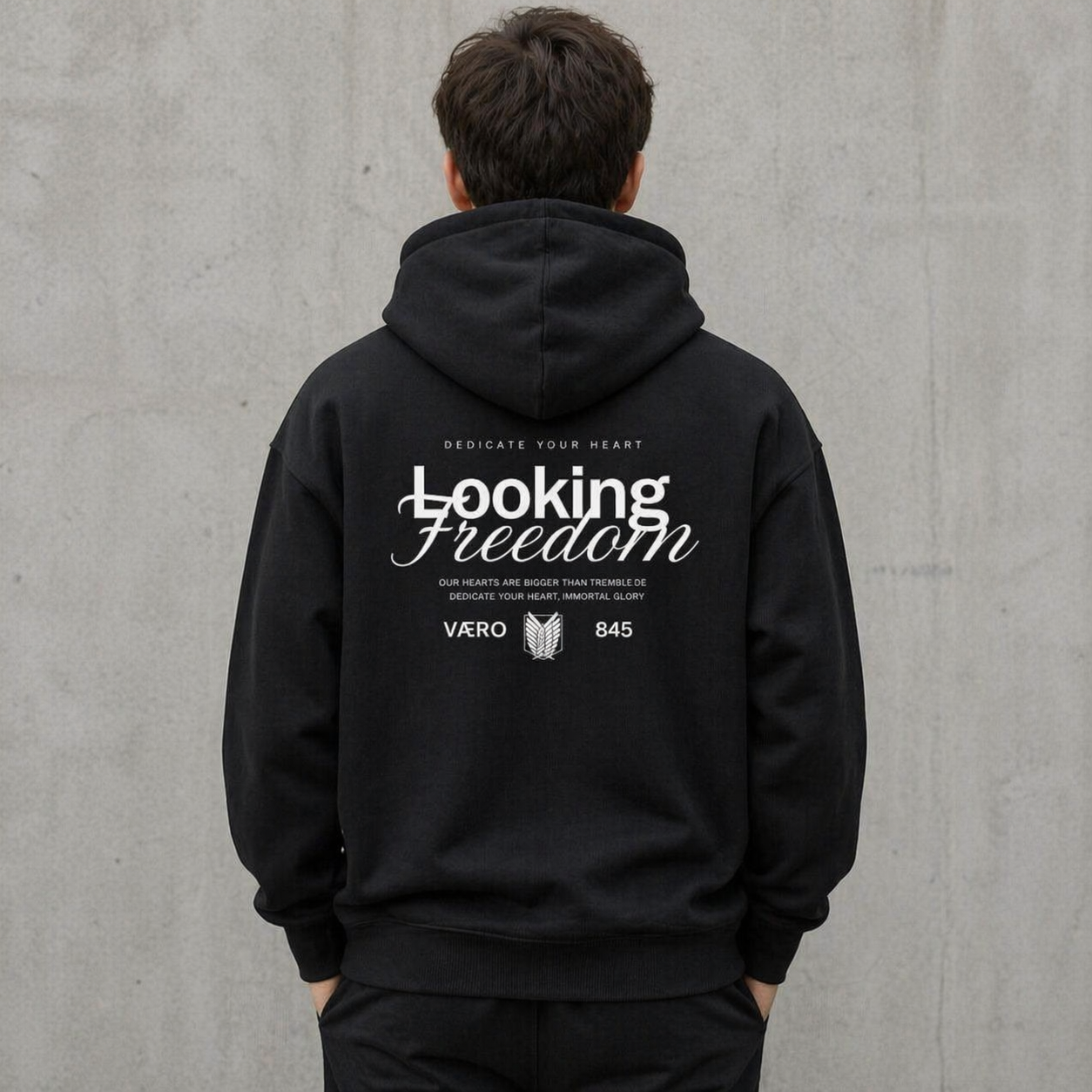 Person wearing a black hoodie with 'Looking Freedom' text on the back against a gray concrete wall.