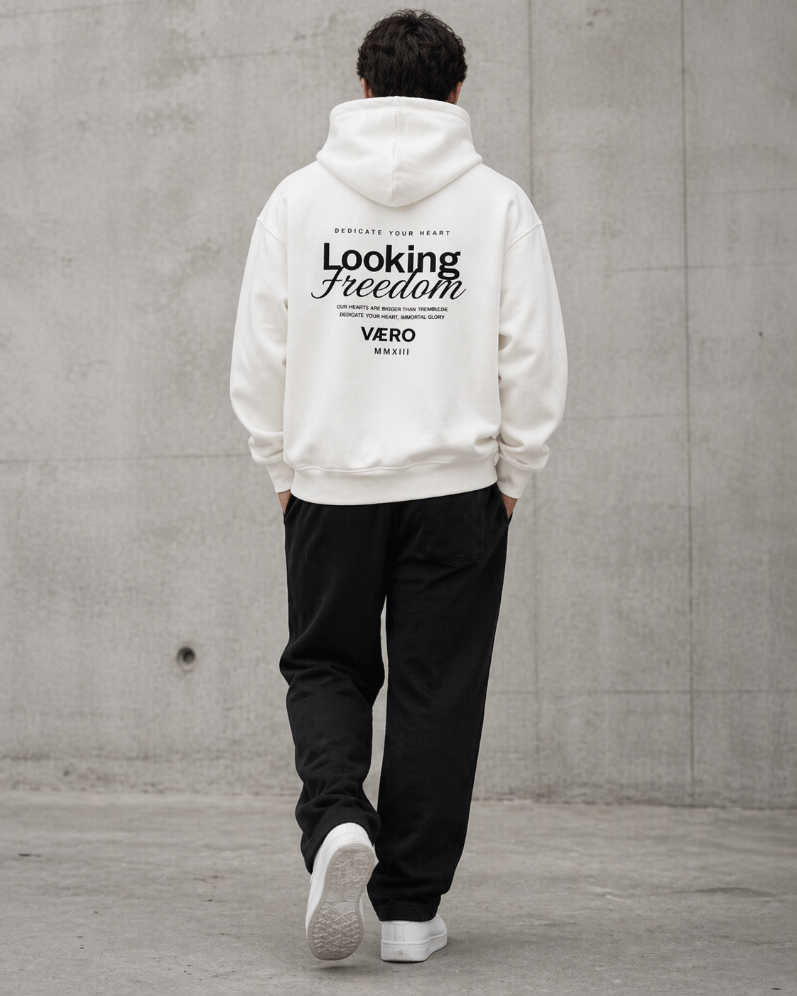 Person wearing a white hoodie with text on the back against a gray concrete wall.