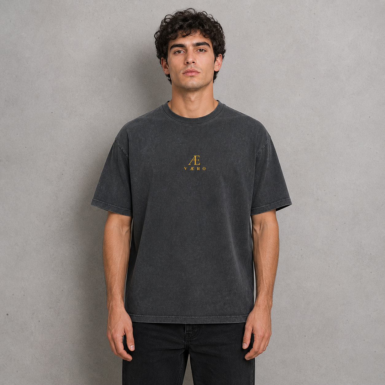 Man wearing a dark gray t-shirt with a logo on a gray background