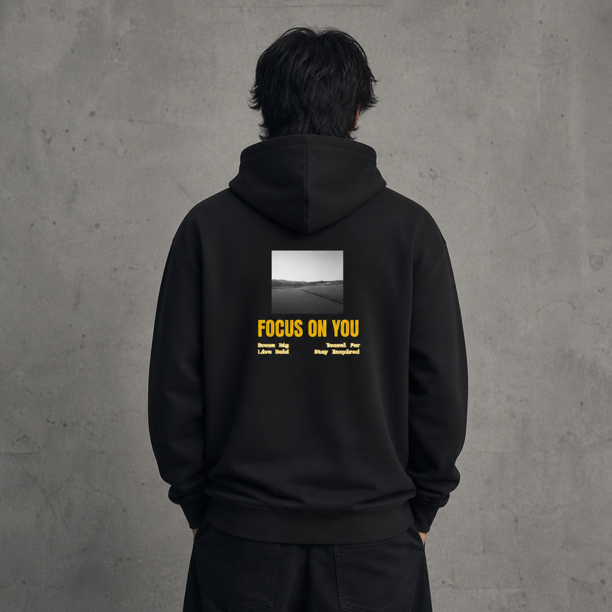 Person wearing a black hoodie with 'FOCUS ON YOU' text on the back against a gray concrete wall.