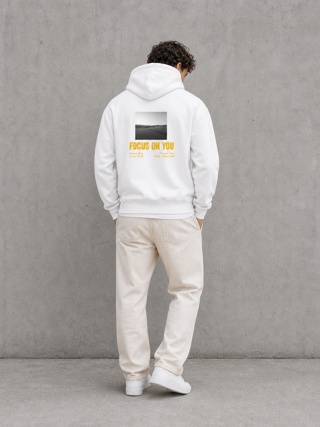 Person wearing a white hoodie with text on the back against a gray wall