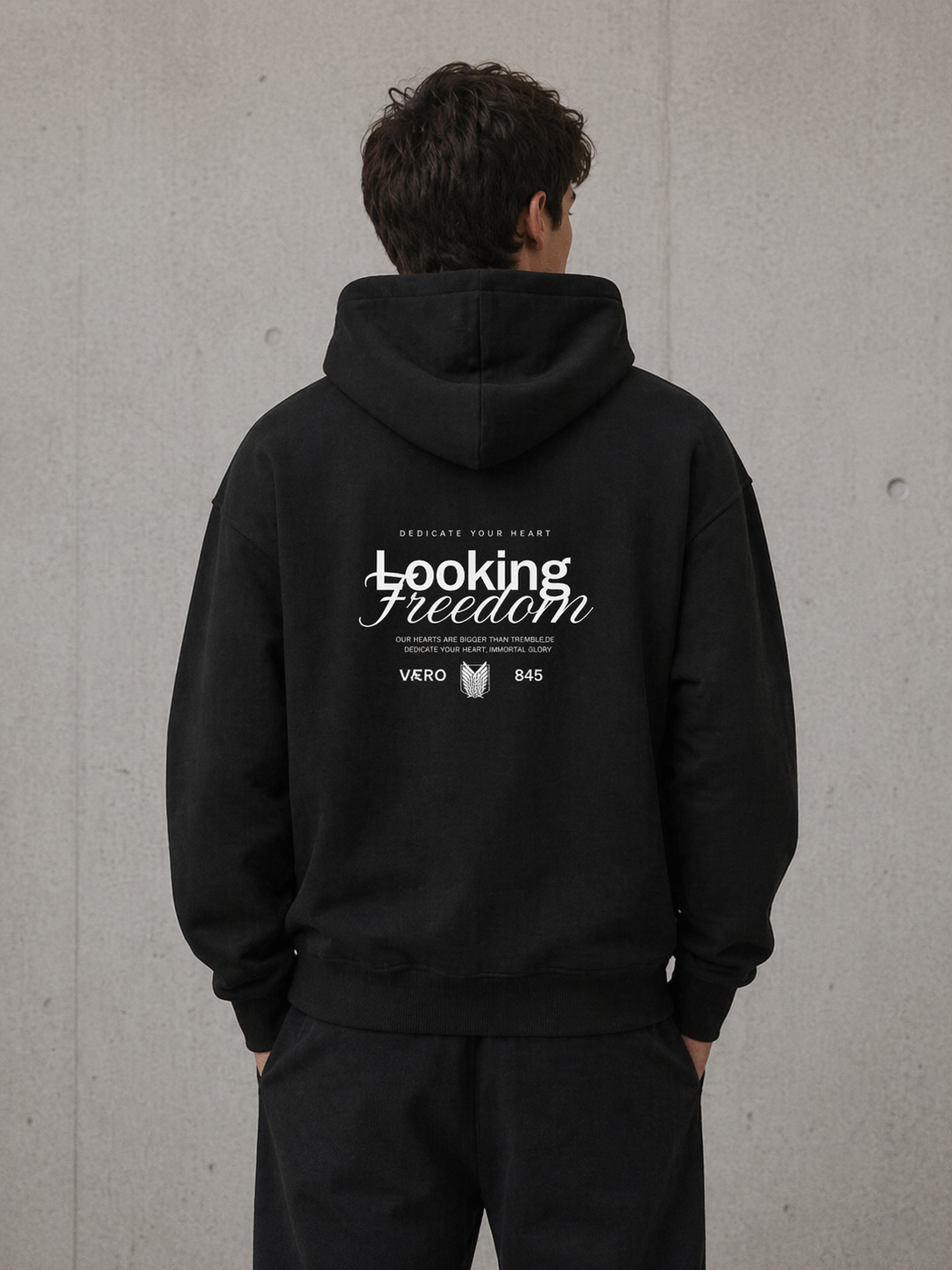 Person wearing a black hoodie with 'Looking Freedom' text on the back against a gray wall.