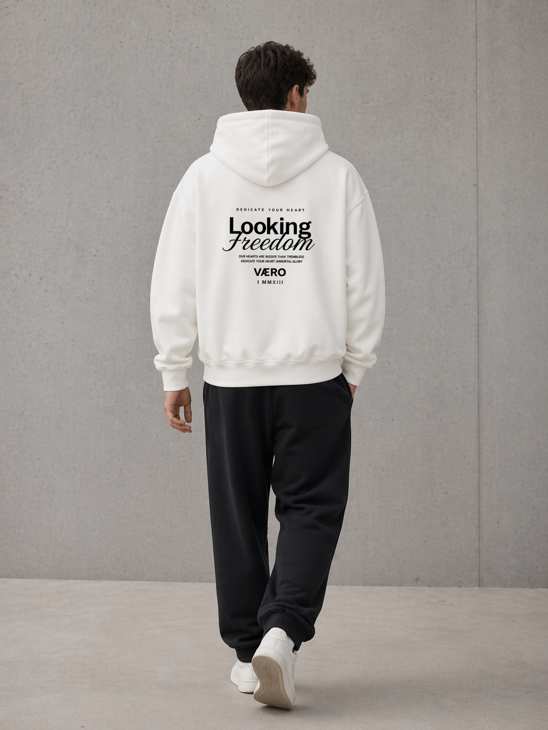Person wearing a white hoodie with text on the back, standing against a gray wall.