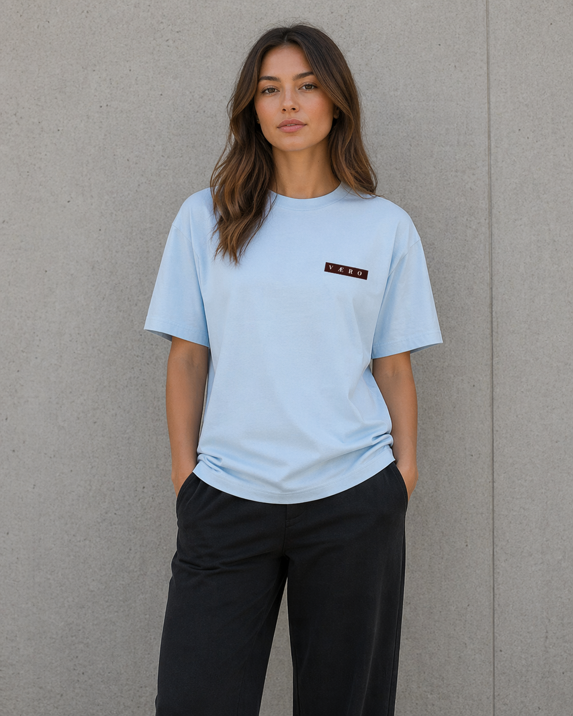 Woman wearing a light blue t-shirt with a small logo on a gray background