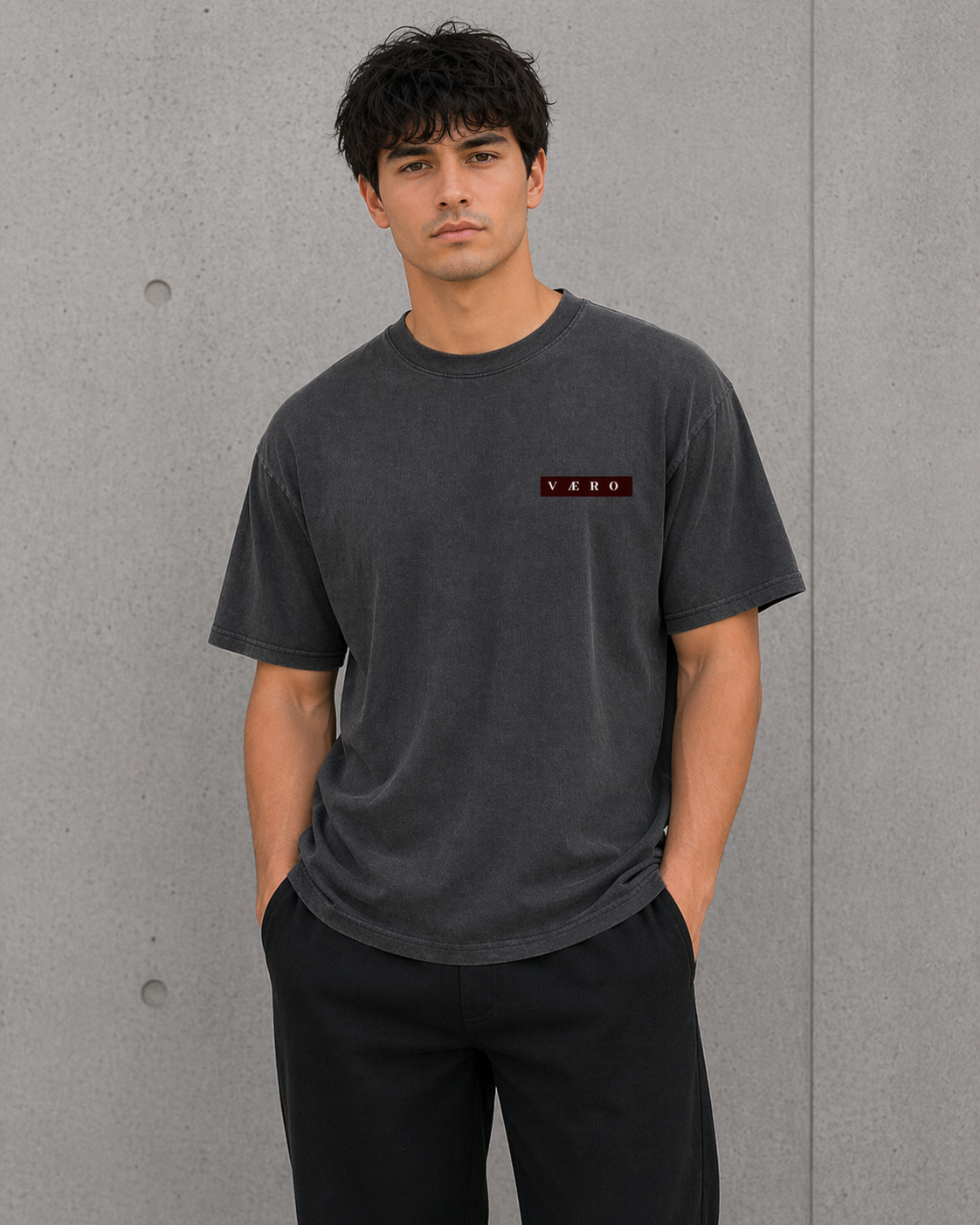 Man wearing a dark gray t-shirt with a logo against a gray concrete wall