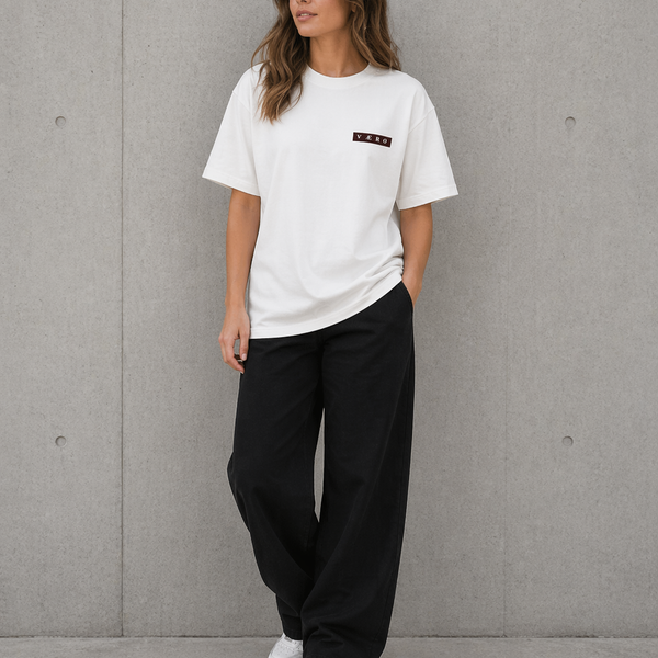 Woman wearing a white t-shirt and black pants against a gray wall