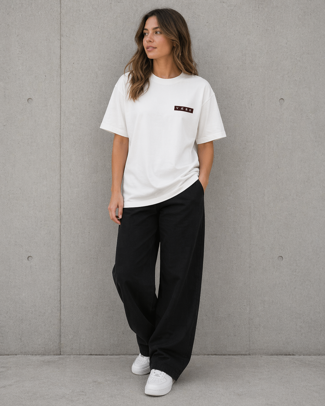 Woman wearing a white t-shirt and black pants against a gray wall