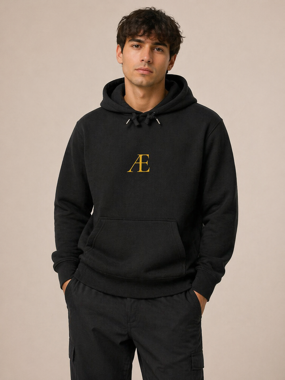 Person wearing a black hoodie with a gold logo on a beige background