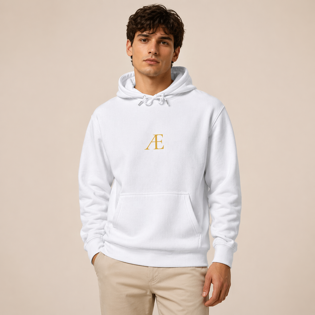 Man wearing a white hoodie with a gold logo on a beige background